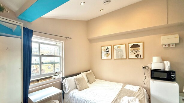 A bedroom with a bed, a desk, a chair, a window, and a microwave.