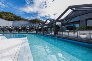 Un área de piscina moderna con agua azul cristalina, rodeada de paredes de vidrio y un suelo de baldosas.