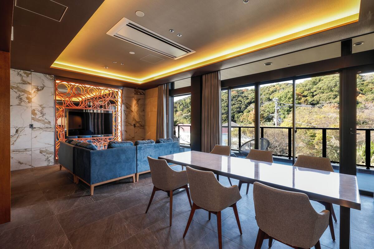 A modern living room with a large TV, blue sofa, and a dining area with a table and chairs.