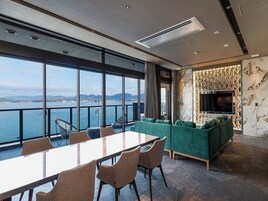 Una habitación moderna con una mesa grande y sillas, un sofá verde, un televisor y vistas al mar.
