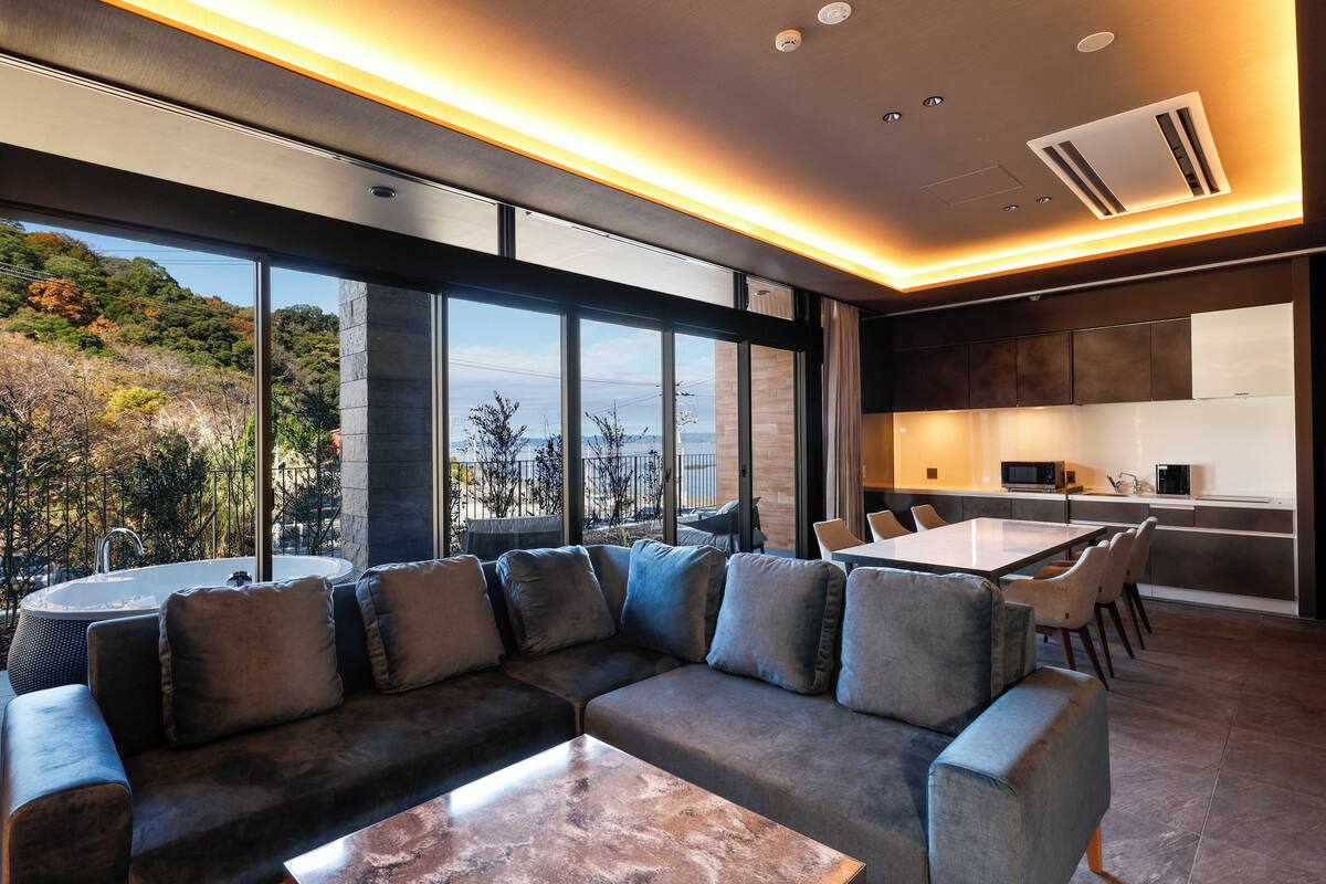 A modern living room with a sectional sofa, a dining table, and a kitchen area with a microwave.