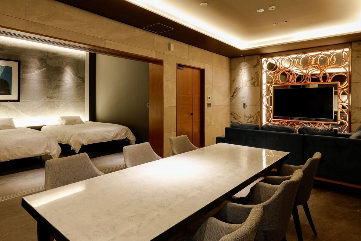 A hotel room with two beds, a dining table, a sofa, and a TV.