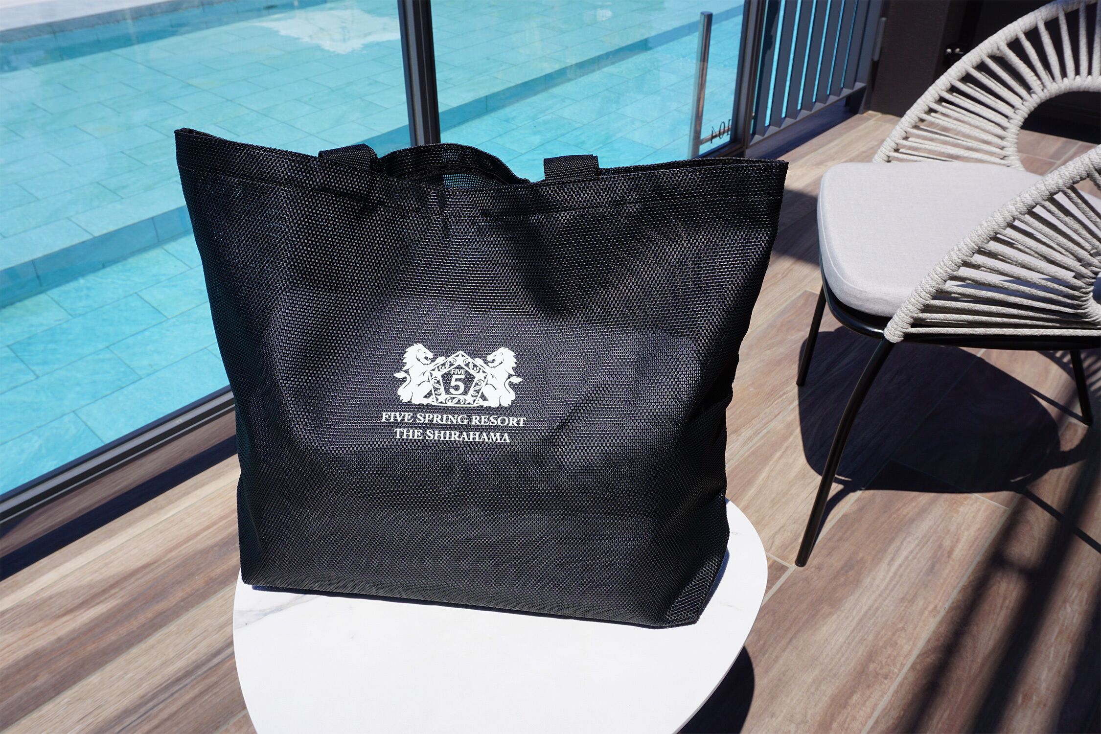 A black bag with a logo on a white table near a pool and wicker chairs.