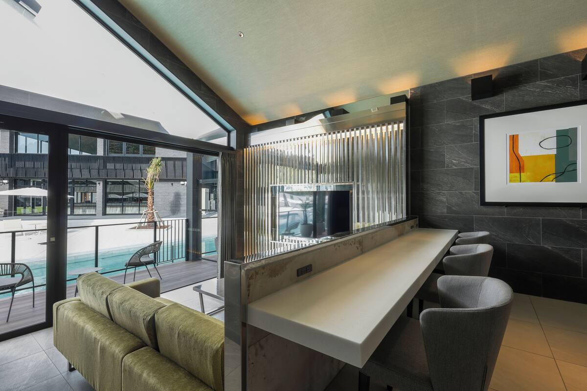 A modern bar area with a long counter, cushioned seating, and a view of an outdoor pool.