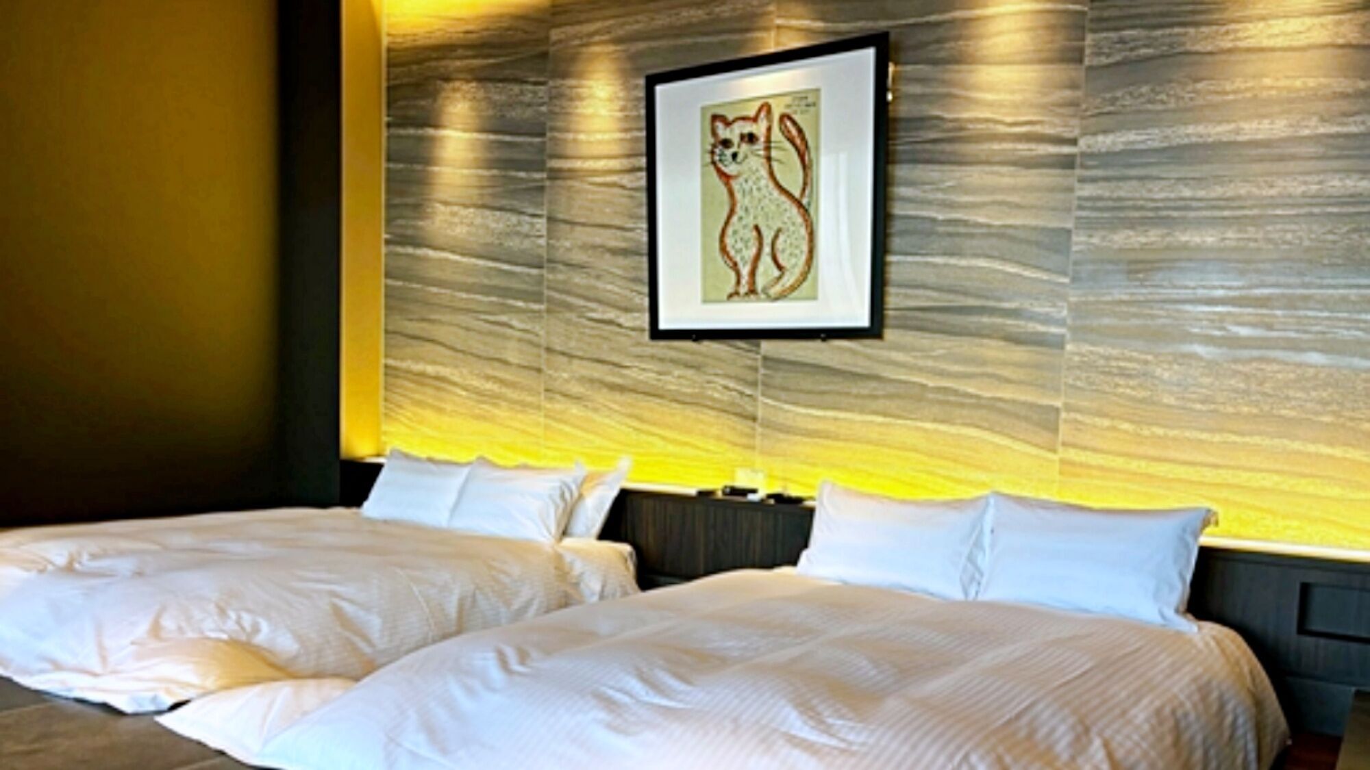 Une chambre d’hôtel avec deux lits, un tableau encadré au mur et un décor mural texturé.