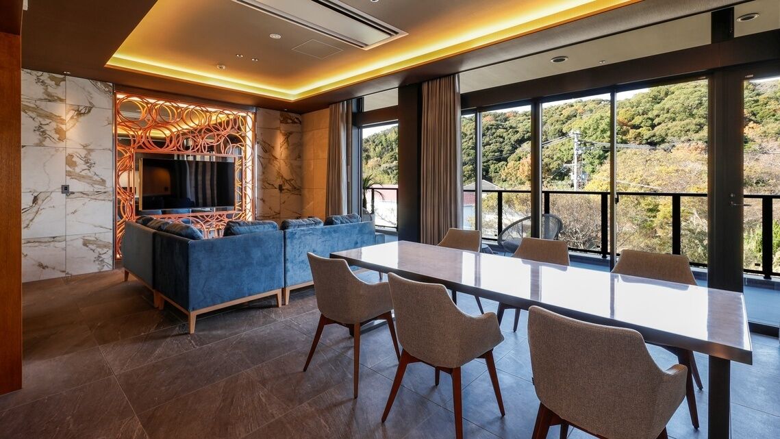 Un intérieur moderne avec une grande table à manger, des canapés et une vue dégagée grâce à de grandes fenêtres.