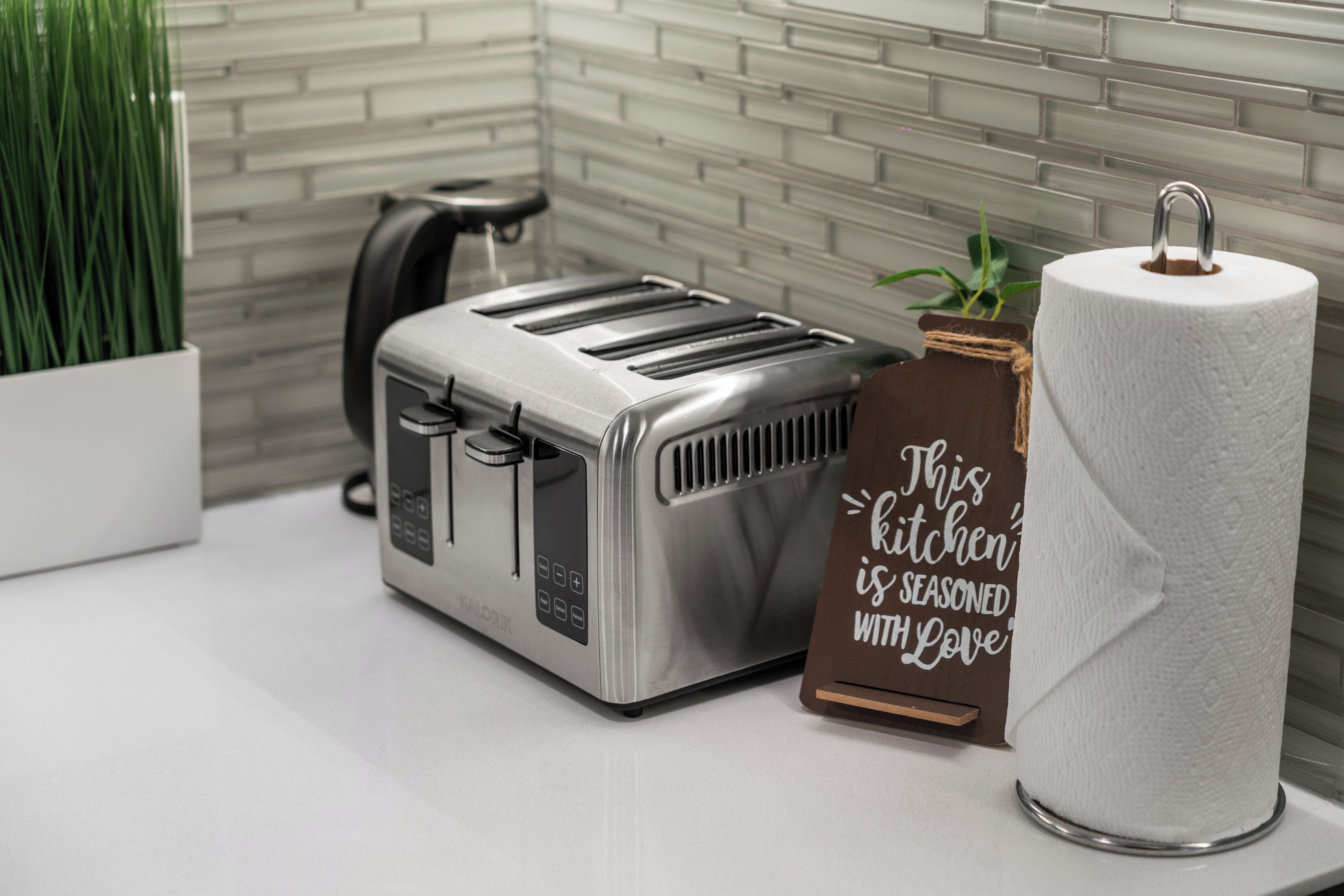 Eine Küche mit einem Toaster, einer Küchenpapierrolle und einem Schild mit der Aufschrift 'Diese Küche ist mit Liebe gewürzt'.