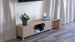 A modern living room with a flat-screen TV mounted on the wall, a wooden console table with a plant, and a woven basket.