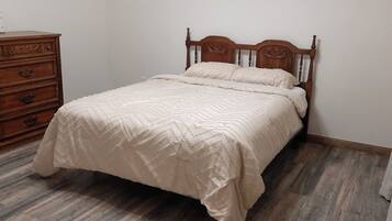 Un dormitorio con estructura de cama de madera, colcha blanca y cómoda de madera con cajones.