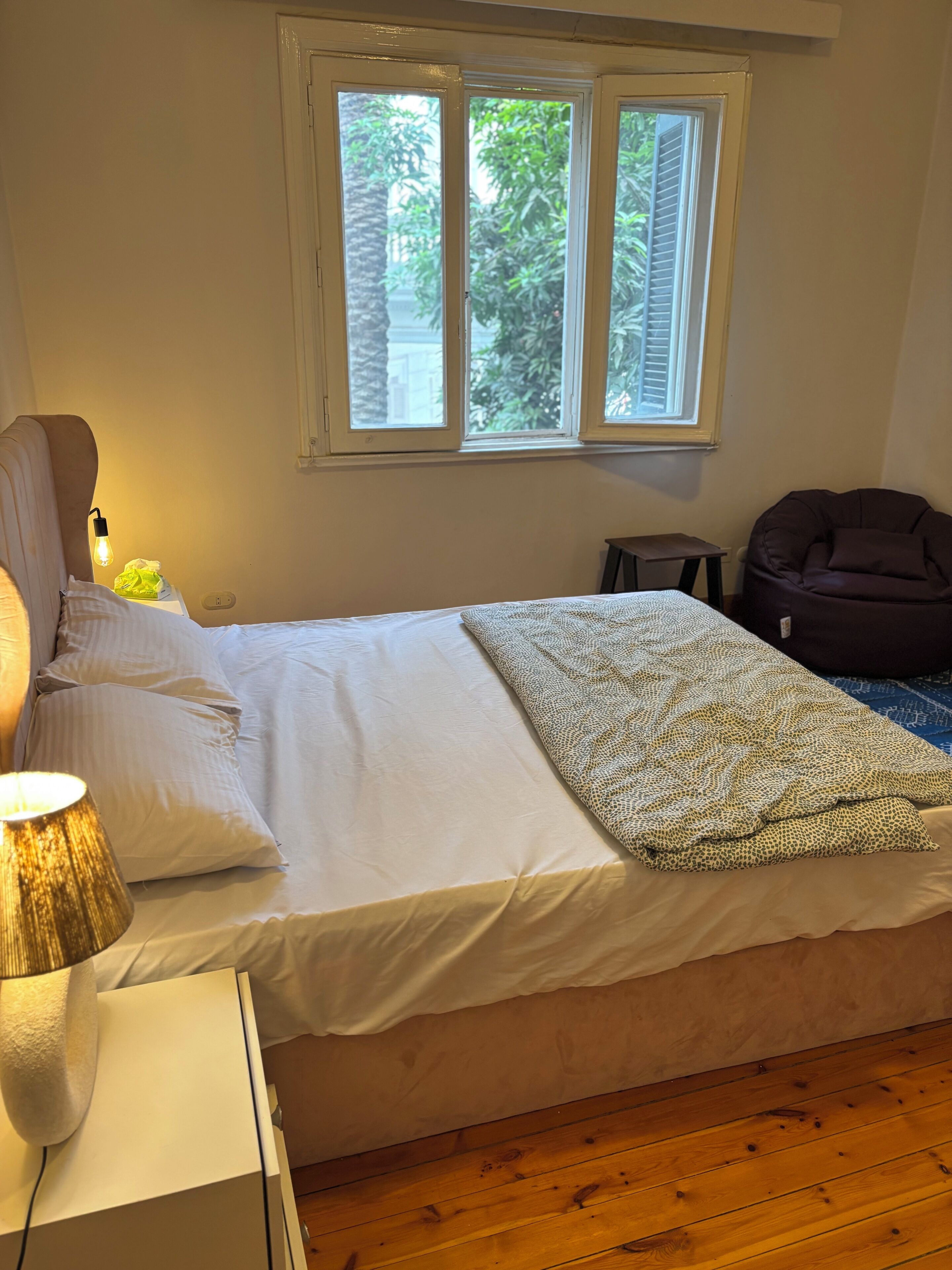 A bedroom with a bed, bedside lamp, window, and a bean bag chair.