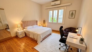 A bedroom with a bed, bedside table, lamp, desk, chair, potted plant, and a window. - Quiet Spacious Room.. Garden City, 2 Min to Nile (Cairo Governorate)