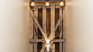 A hallway with a wooden wall panel featuring a mounted animal skull, a ceiling light fixture, and a door with a window showing a mountain view. - Escape to The Adventure Inn Yellowstone- Absaroka, just a minute from the park! (West Yellowstone)