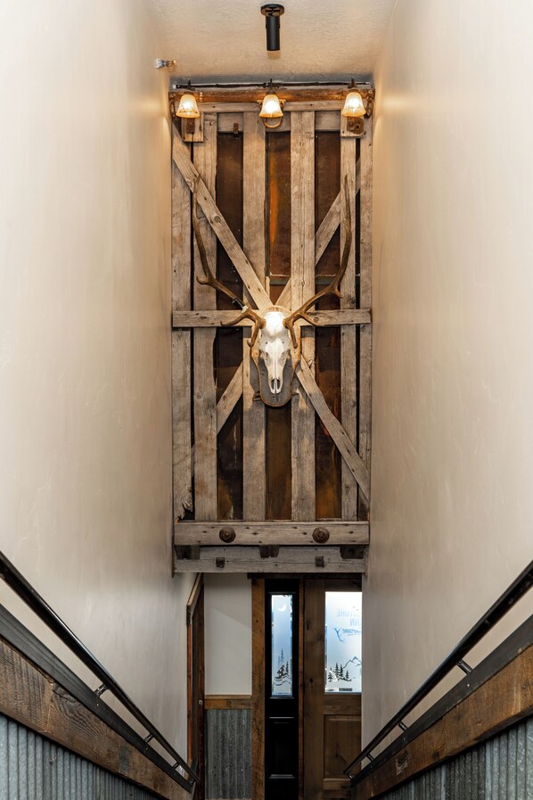 A hallway with a wooden wall panel featuring a mounted animal skull, a ceiling light fixture, and a door with a window showing a mountain view.