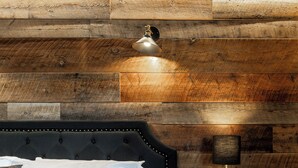 A bedroom with a tufted headboard, a bedside lamp, and a wooden wall panel. - Escape to The Adventure Inn Yellowstone- Absaroka, just a minute from the park! (West Yellowstone)
