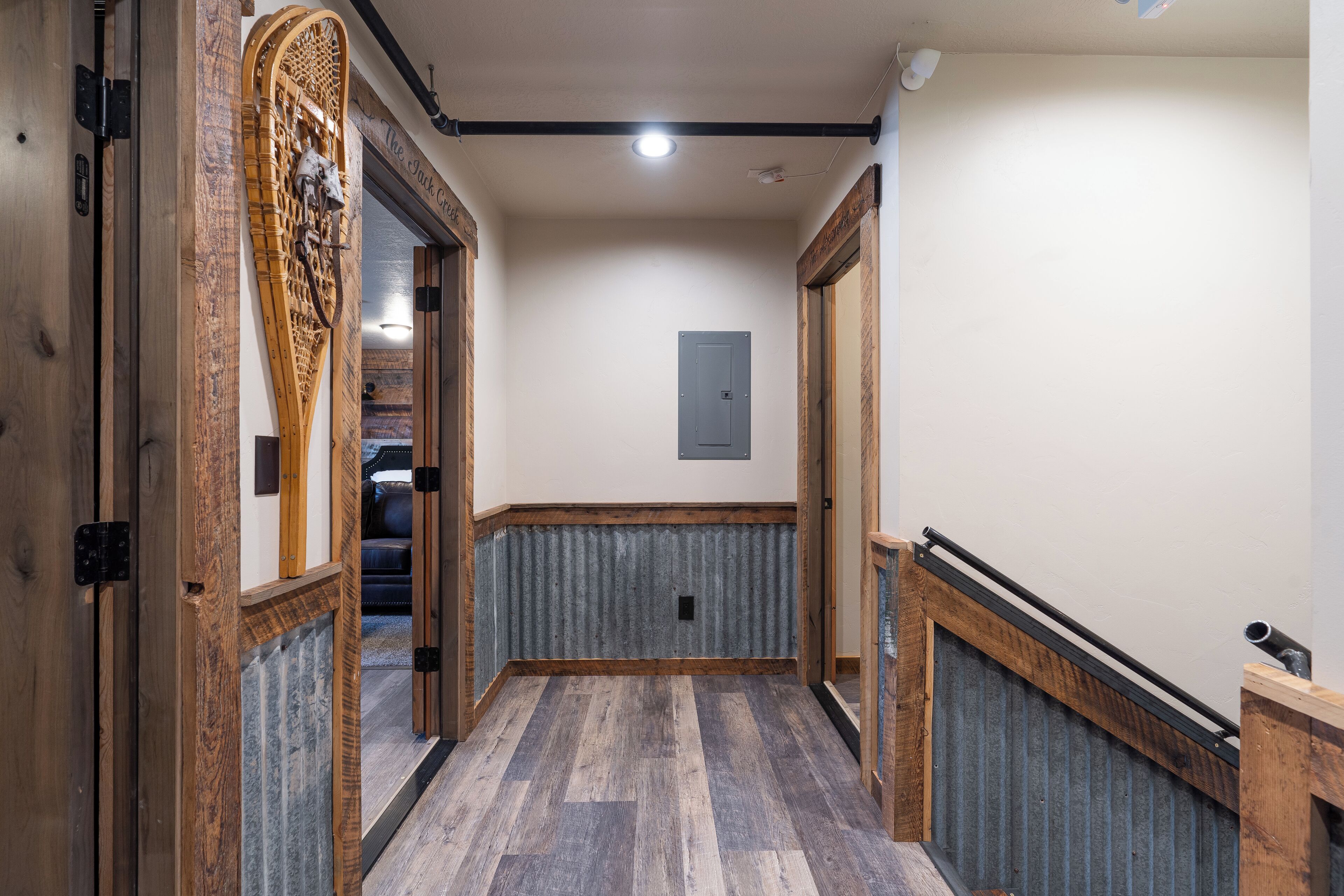 A hallway with wooden flooring, a metal handrail, and a door with a wooden frame.