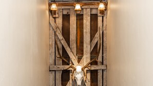 Een hal met houten lambrisering, waarop een opgeplakt dierenschedel en drie wandlampen bevestigd zijn.