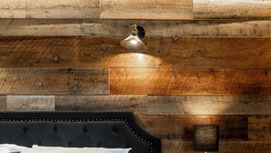 Un lit avec du linge de lit blanc, une tête de lit capitonnée de couleur sombre et une table de chevet avec une lampe.