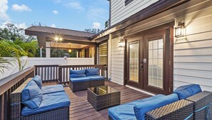 An outdoor deck with wicker furniture and a glass-top table, a covered area with a roof, and a door with a window. - Habana Luxury Bungalow- Heated pool (Tampa)