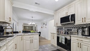 A kitchen with white cabinetry, a black and white patterned backsplash, stainless steel appliances, and a black countertop. - Habana Luxury Bungalow- Heated pool (Tampa)
