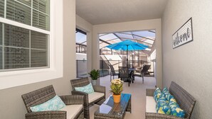 Un patio ensoleillé, agrémenté de meubles en osier, d’un parasol bleu et d’une pancarte de bienvenue.