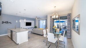 Une cuisine moderne dotée d’un îlot central, de meubles blancs et d’un coin repas avec une table et des chaises en verre.