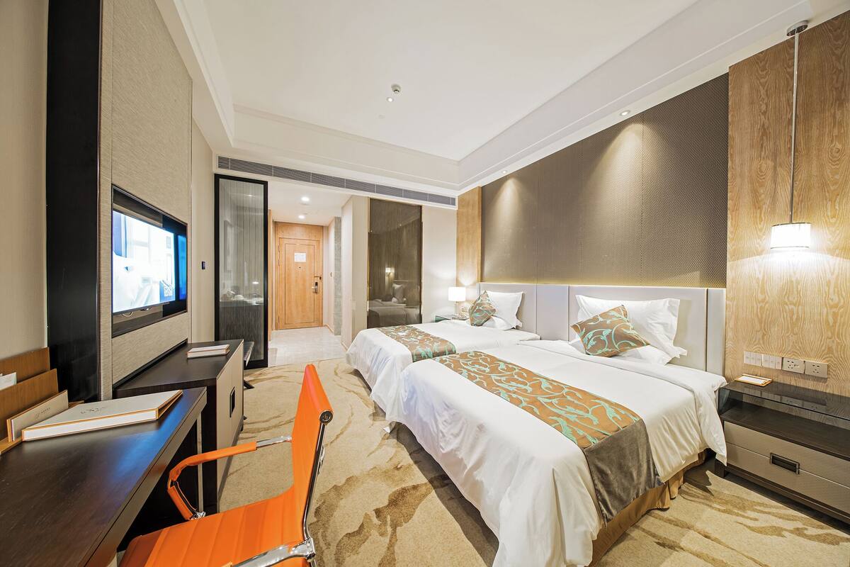 A hotel room with two beds, a desk, a TV, and a bathroom visible through an open door.