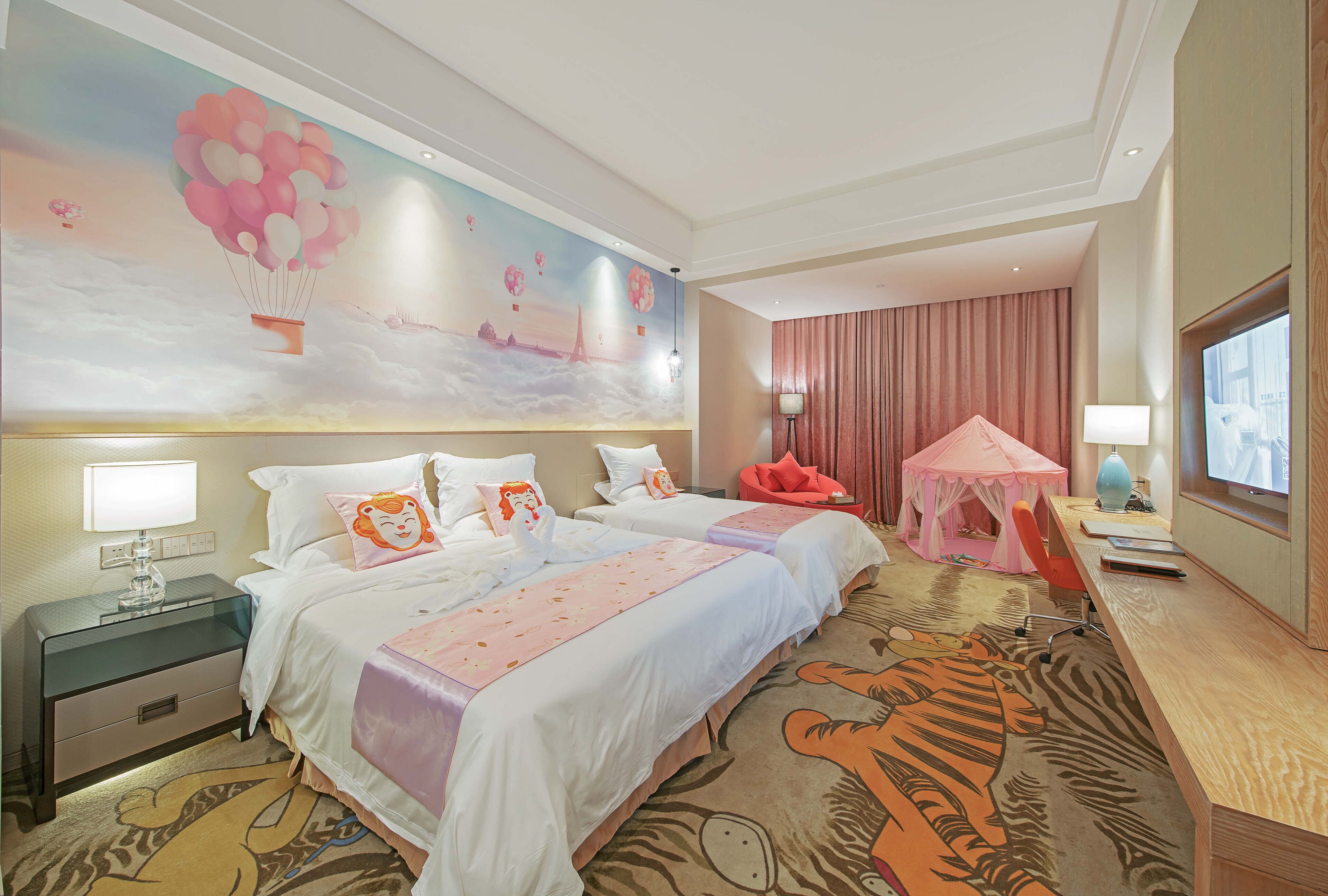 Una habitación de hotel con dos camas, un escritorio, un televisor y un mural de globos aerostáticos.