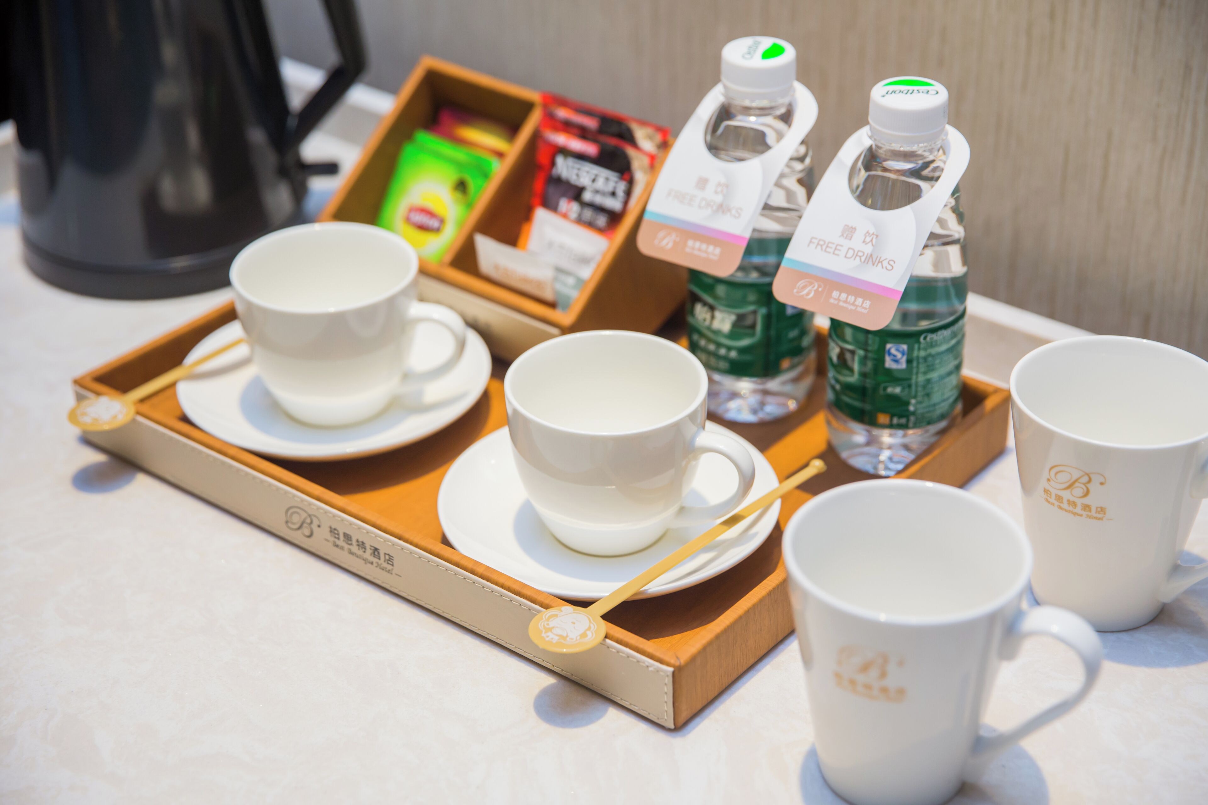 Una bandeja con tazas y platillos blancos, dos botellas de agua y una caja de té.