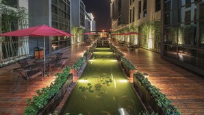 A nighttime outdoor area with a water feature, seating, and tables under red umbrellas. - Best Boutique Hotel (Shanghai)