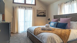 A bedroom with a bed, a dresser, a window with curtains, a painting on the wall, and a lamp.