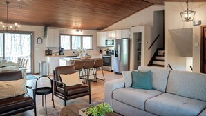 A spacious living area with a sofa, chairs, and a coffee table. A kitchen with modern appliances and a dining area with a table and chairs is visible in the background.