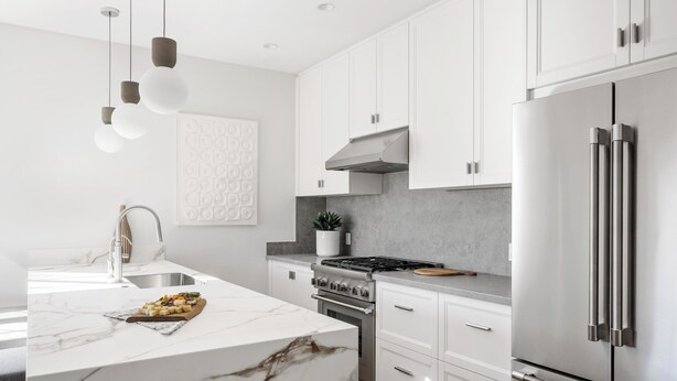 Een moderne keuken met witte kasten, een marmeren eiland, roestvrijstalen apparatuur en hangende lampen.
