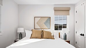Een keurig opgeruimde slaapkamer met een groot bed, twee nachtkastjes, een raam met uitzicht en een deur.
