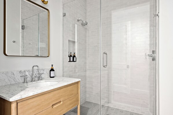 A modern bathroom with a marble sink, a large mirror, a glass shower enclosure, and a wooden vanity. - 2-bedroom - WiFi, AC, garage parking with EV charger. (Solvang)
