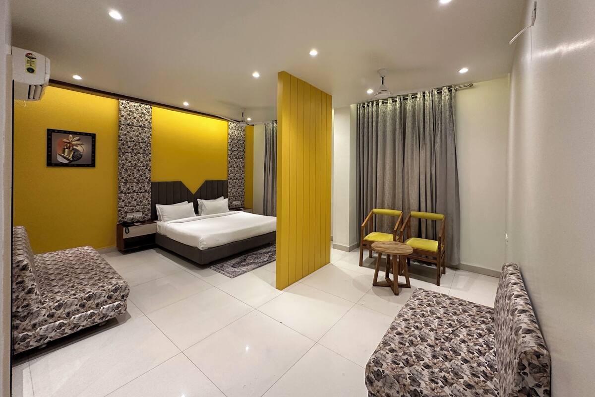 A modern bedroom with a bed, two chairs, a nightstand, and a large window with curtains.