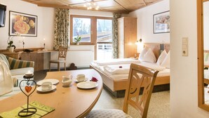 A cozy hotel room with a wooden ceiling, a bed with white linens, a dining table with tea set, and a window with a view of the outside.