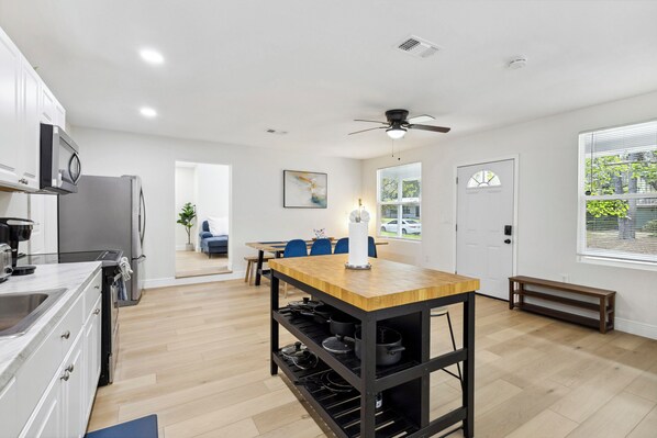 Une cuisine moderne avec un îlot central, un coin repas avec des chaises bleues et une vue sur l’extérieur.