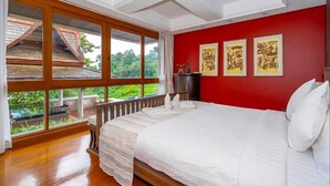 Une chambre avec un grand lit, un plancher en bois et une vue sur la verdure grâce à de grandes fenêtres.