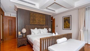 Une chambre d’hôtel avec un grand lit, un lit plus petit, une tête de lit en bois, une table de chevet, une lampe, un élément décoratif mural et un tableau encadré.