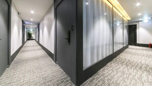 A modern hotel hallway with a carpeted floor, glass doors, and recessed lighting. - STAY SANGMU (Gwangju)