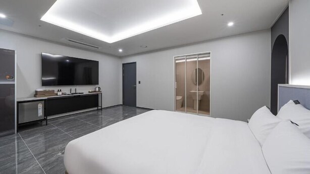 A modern hotel room with a large bed, a flat-screen TV, a vanity with a mirror, and a walk-in closet. - STAY SANGMU (Gwangju)
