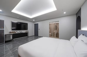 Quarto de hotel moderno com uma cama grande, televisão de tela plana, penteadeira com espelho e closet espaçoso.