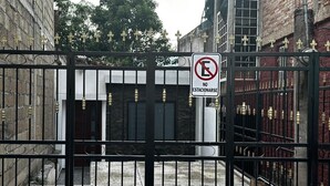 Une entrée fermée par un portail, agrémentée d’un panneau indiquant « Stationnement interdit », un portail en métal et un bâtiment à la façade en briques.
