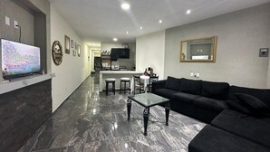 Un salon moderne avec un canapé noir, une table basse en verre et un téléviseur posé sur un sol en marbre.