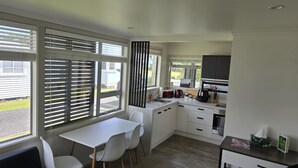 A modern kitchen with white cabinets, a dining area with a white table and chairs, and large windows with blinds.