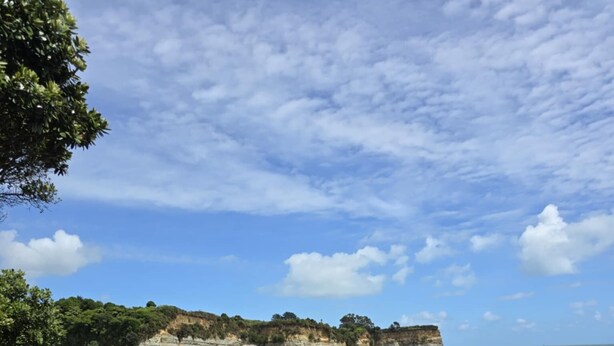 A rocky shoreline with large boulders and a cliff in the background.