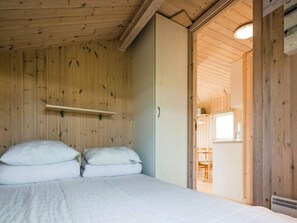 A wooden room with a bed, a shelf, and a door leading to another room.