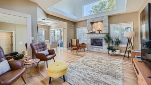 Un salon spacieux avec une cheminée, des fauteuils en cuir, un pouf jaune et un téléviseur.