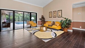 Un vaste salon doté d’une grande porte-fenêtre coulissante donnant sur une piscine, d’un canapé jaune et d’une table basse ronde.