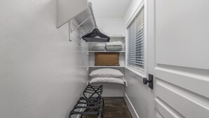 Un pasillo estrecho con una puerta blanca, un ventanal con persianas, un tendedero de pared y un pequeño banco.